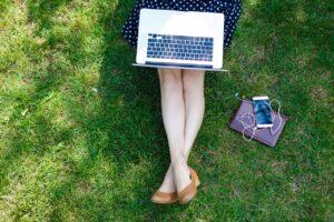 Single lady in polka dot dress sitting on the grass with a laptop on her lap